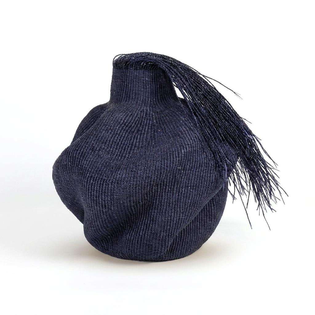 Hairy black wavy sculptural basket with a long fringe falling from its collar, on white