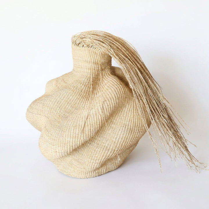 Hairy natural wavy sculptural basket with a long fringe sweeping from its collar, on white