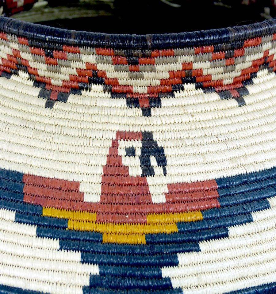 Close-up of intricate macaw feather weaving detail showing natural dye colors in Wounaan palm fiber basket