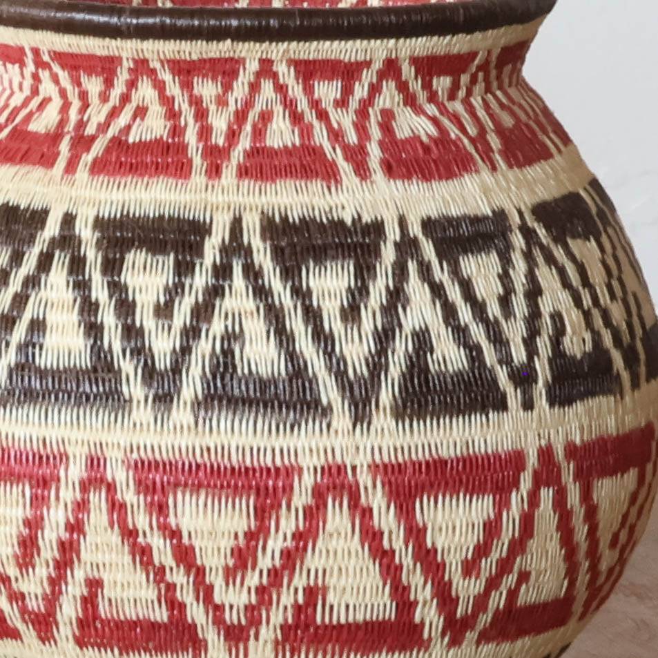 Close-up detail of tight palm fiber weaving showing crimson dyed strands in geometric triad pattern