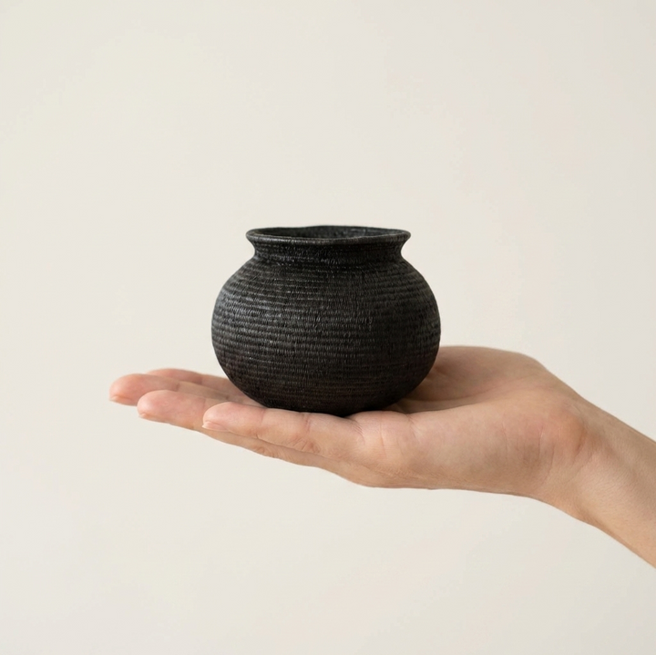 Small black handwoven Wounaan basket held in hand showing miniature scale, about three inches tall
