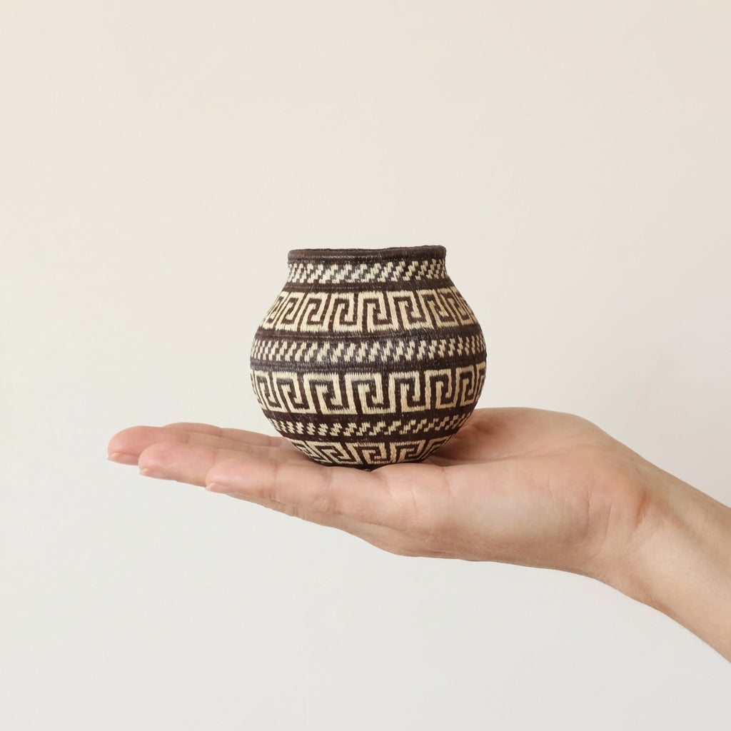 Small woven basket with a brown and cream maze pattern held in an open hand