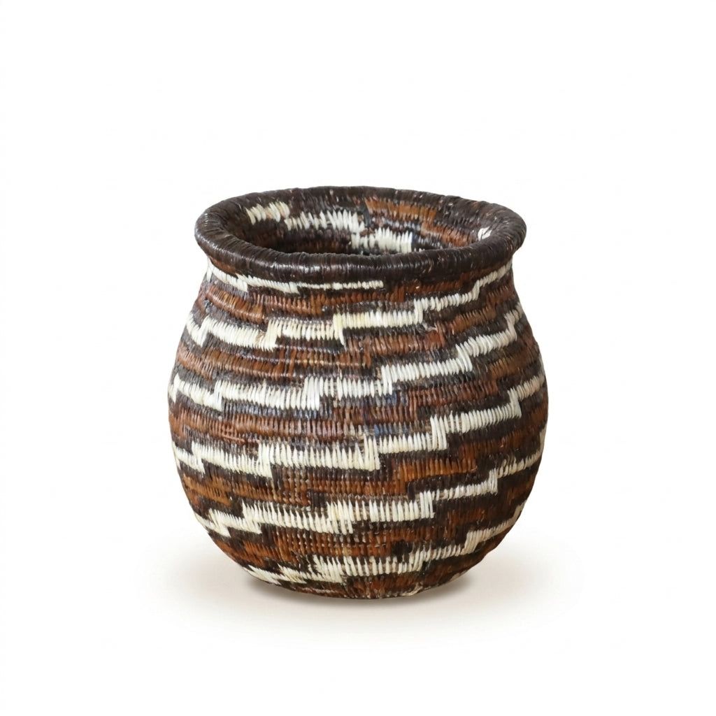 Close view of miniature Wounaan basket showing diagonal staircase swirl in warm brown, rust and ivory palm fiber