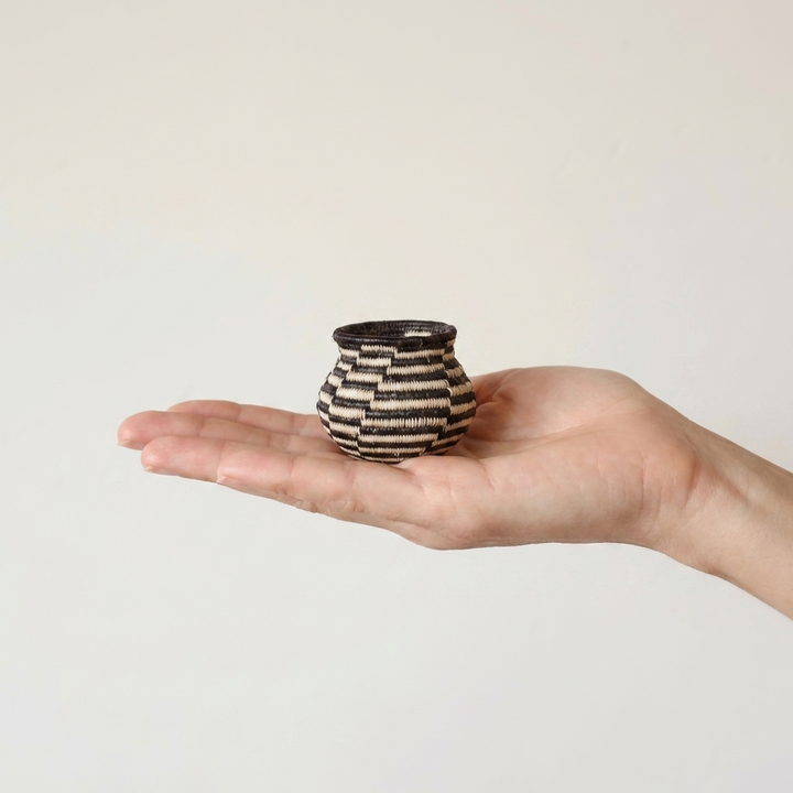 Tiny black and white swirl Wounaan basket held in hand showing miniature scale, about two inches across