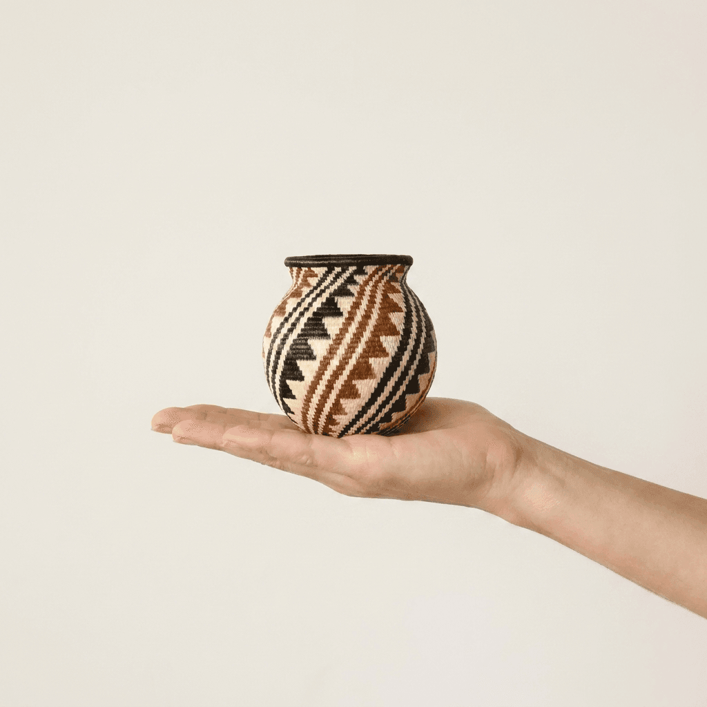 Black, rust and cream spiral Wounaan basket held in hand showing miniature scale, about three inches tall
