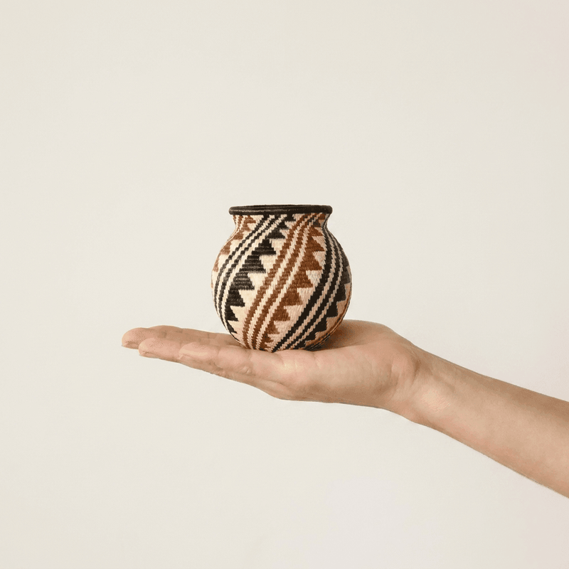 Black, rust and cream spiral Wounaan basket held in hand showing miniature scale, about three inches tall