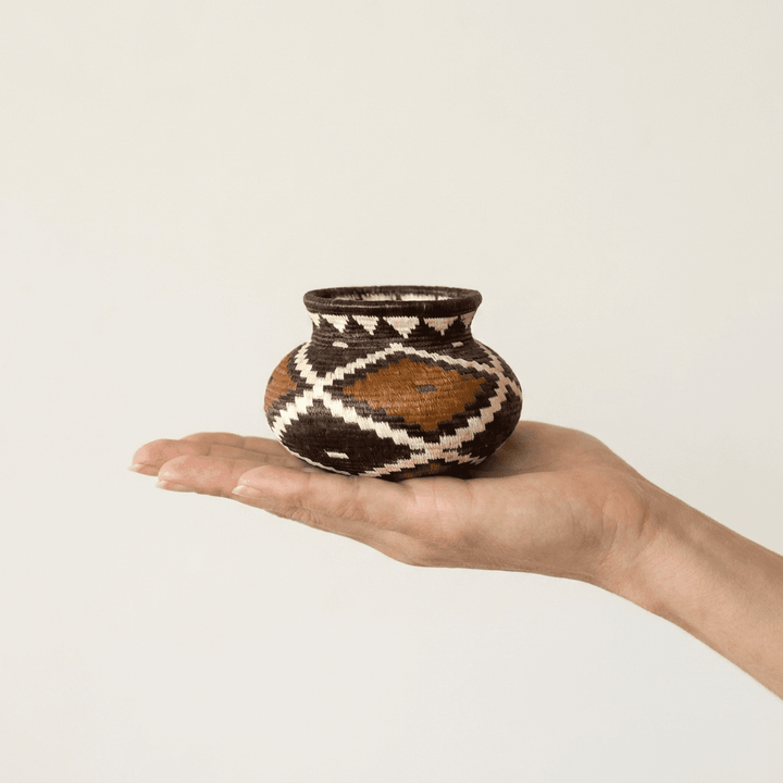 Tiny geometric Wounaan handwoven basket held in hand showing miniature scale, rust and black diamonds