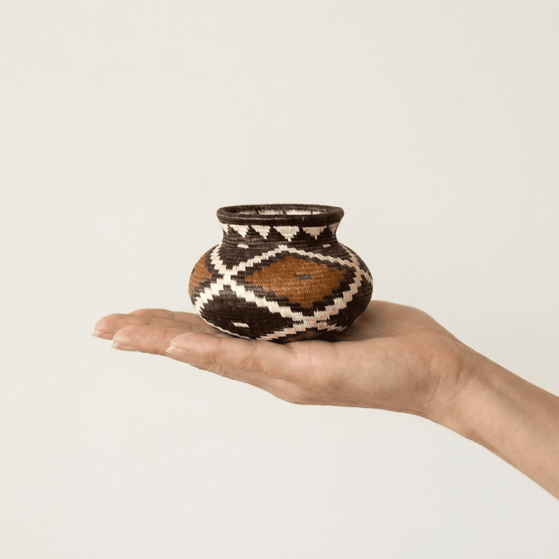 Tiny geometric Wounaan handwoven basket held in hand showing miniature scale, rust and black diamonds