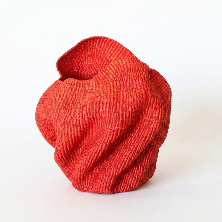 Red wavy sculptural basket with folded undulating walls, on white