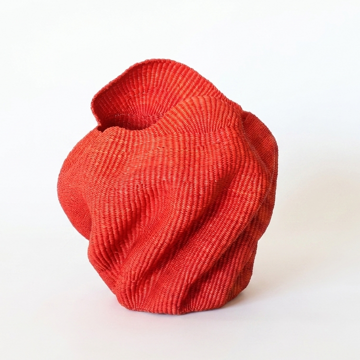 Red wavy sculptural basket with folded undulating walls, on white