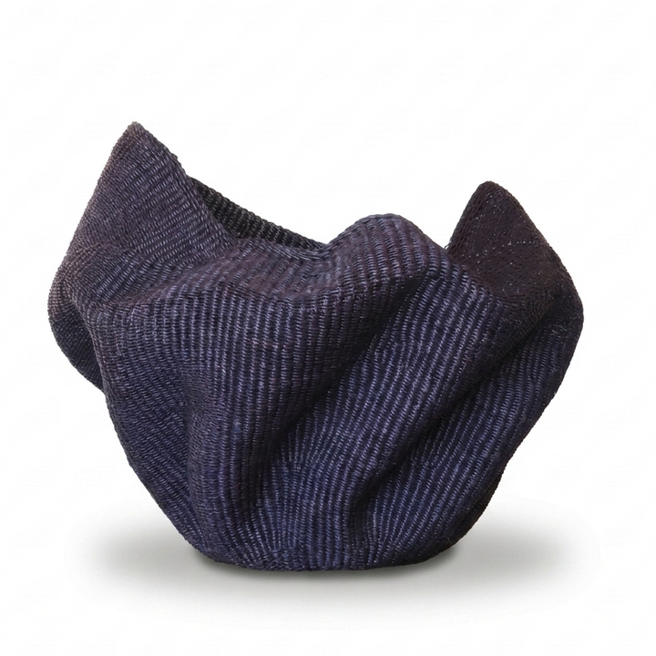 Sculptural dark indigo woven vessel with draped folds, angled view on white