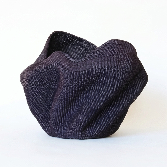 Sculptural dark indigo woven vessel with folded peaks on a white background