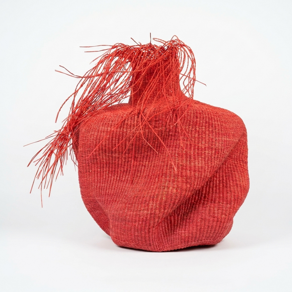 Sculptural red woven vessel with a spiky red fringe, angled view on white