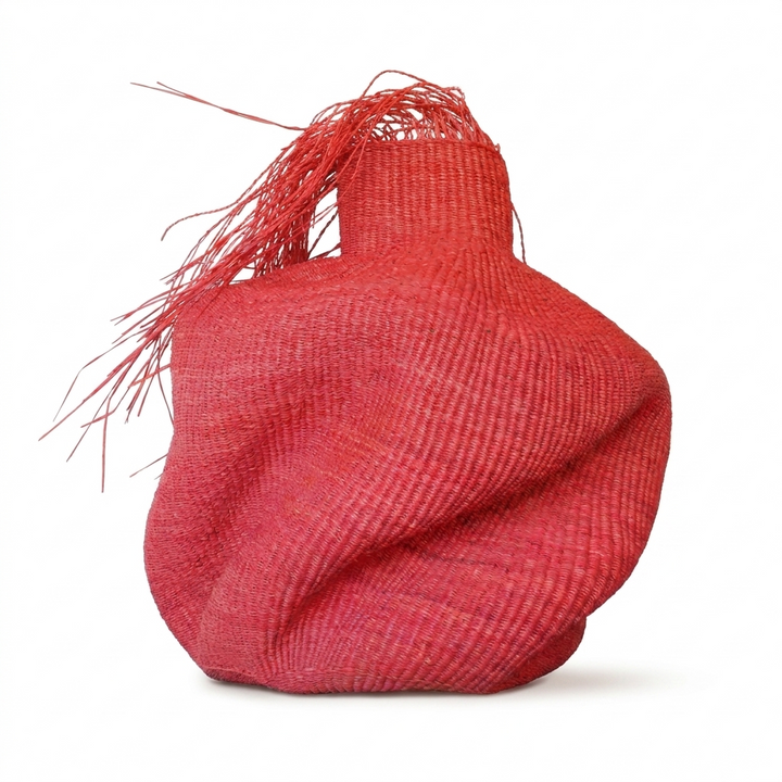 Sculptural red woven vessel with a wild red fringe on top, on white