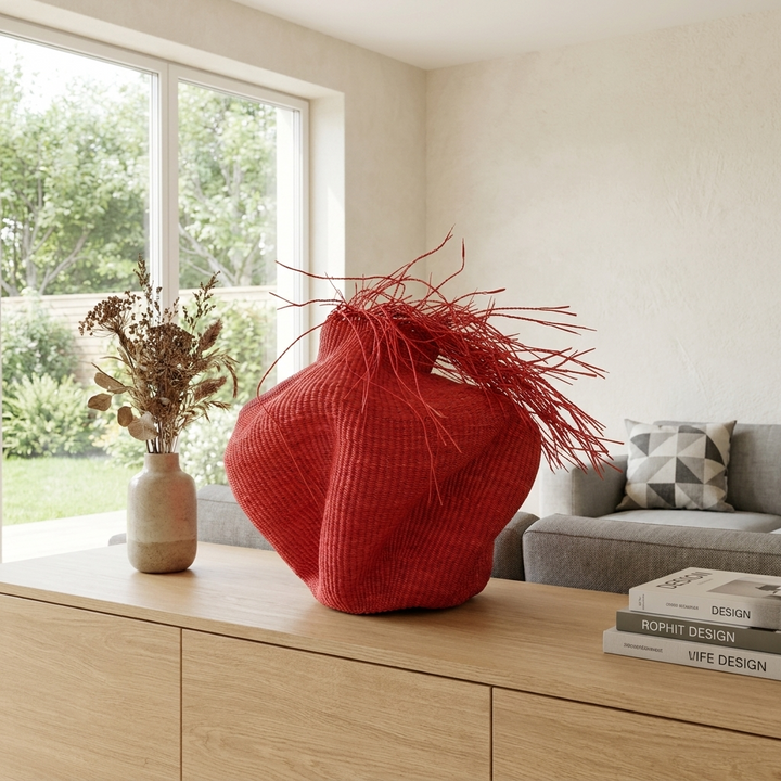 Sculptural red fringed woven vessel on a console beside a window