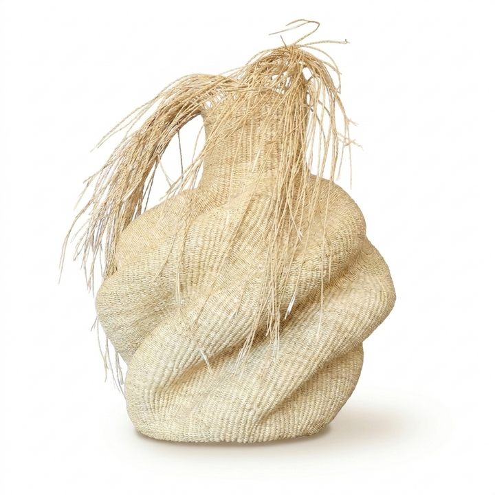 Sculptural natural woven vessel with a shaggy raffia fringe on top, on white