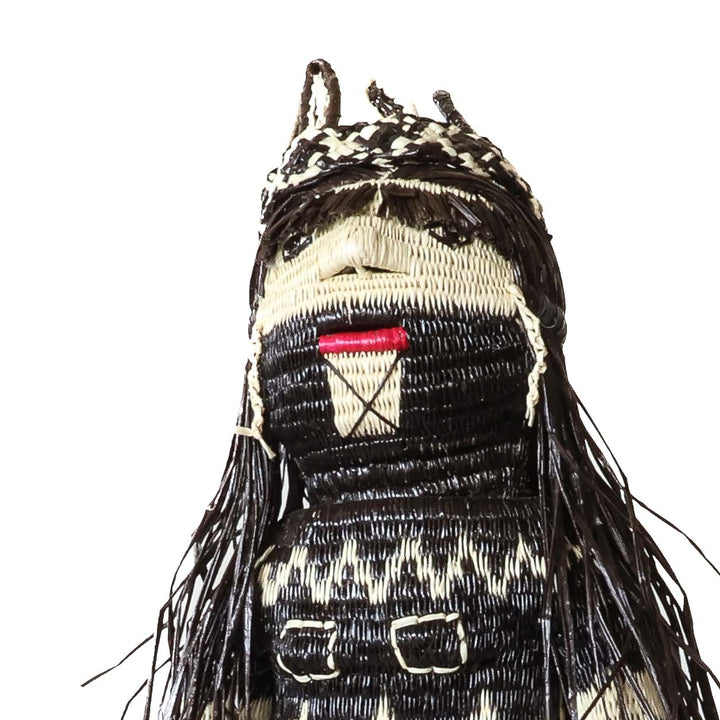 Close-up of a woven Embera doll's head with black and cream fiber hair and a beaded face