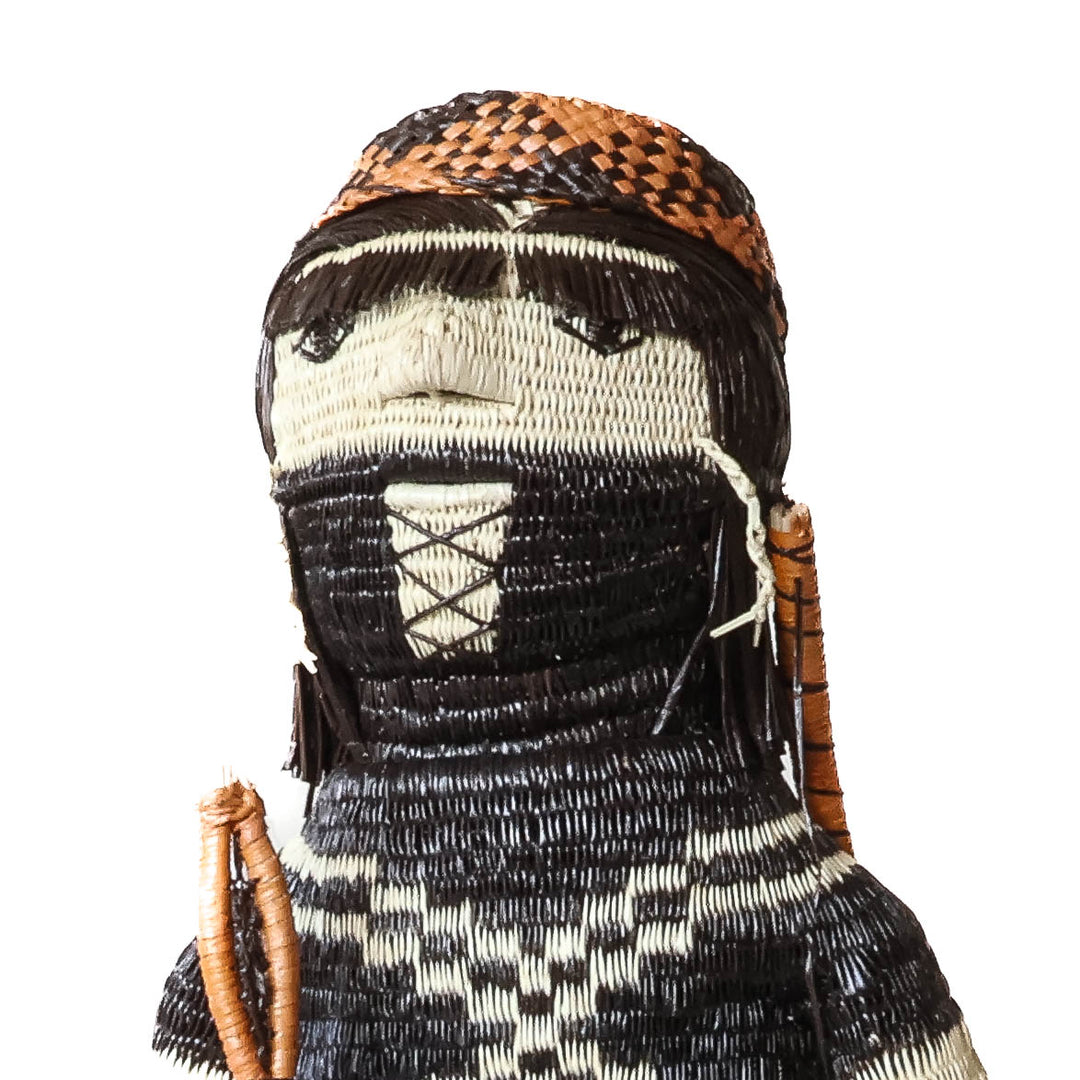 Close-up of a woven Embera doll's head with a beaded headband and a black and cream face