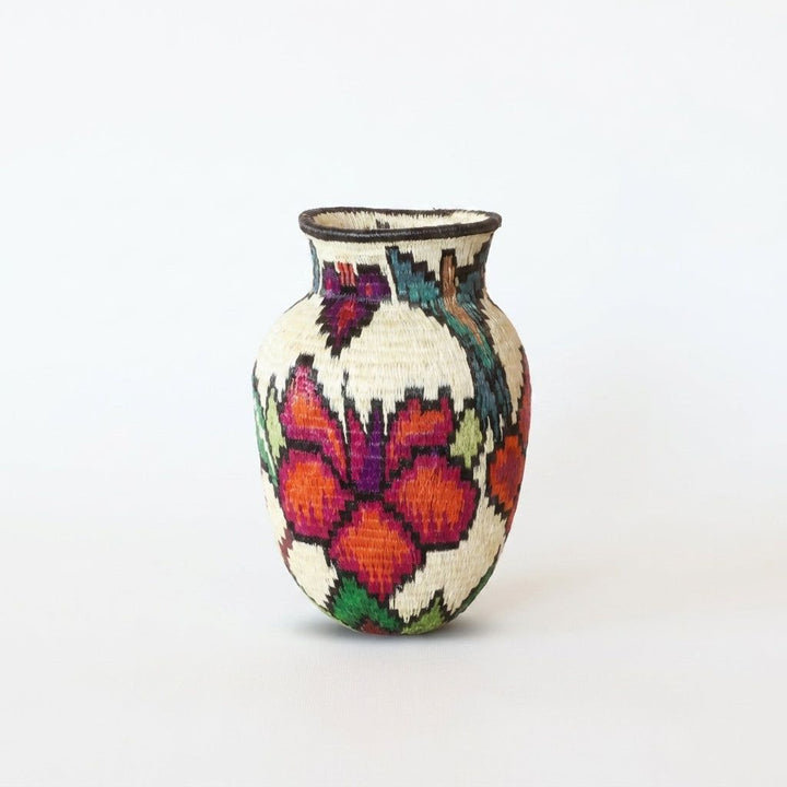 Magenta and orange butterfly with purple body above red blooms on mini Wounaan handwoven basket, Panama