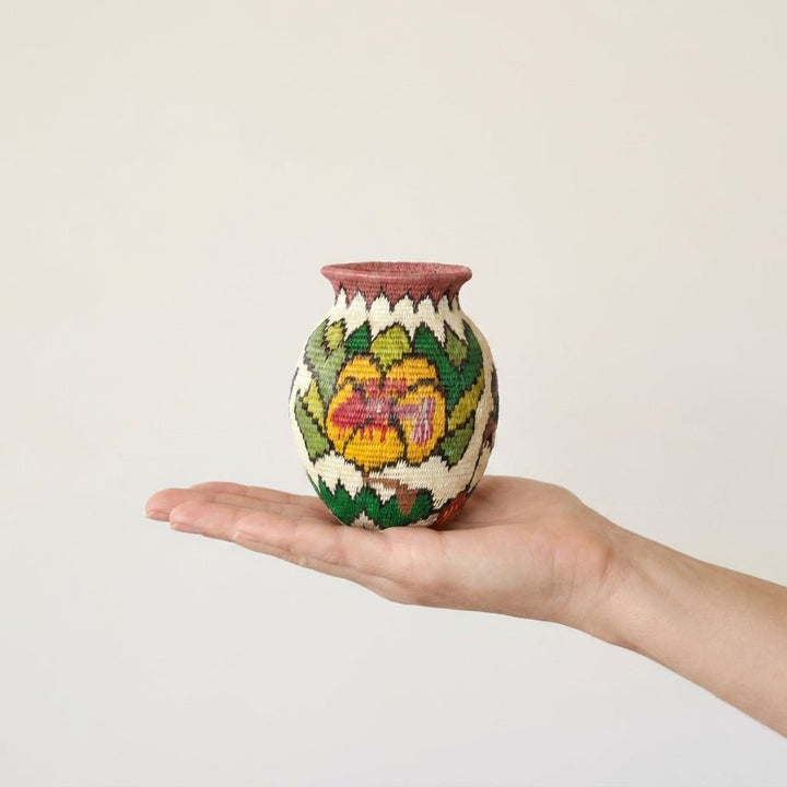 Mini Wounaan handwoven floral basket held in hand showing miniature scale, golden blossom and rose rim