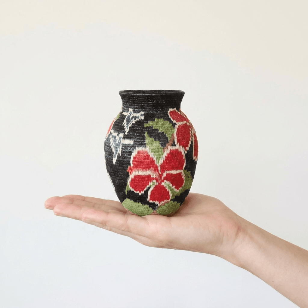 Mini Wounaan handwoven night-garden basket held in hand showing miniature scale, red hibiscus on black