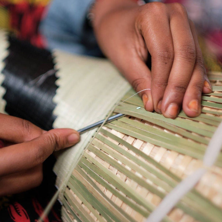 Close-up of a Rwandan artisan's hands stitching the rim of a dark coiled basket with a needle