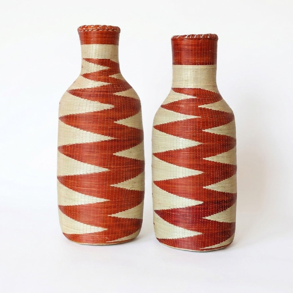 Pair of tall woven bottle vessels with red and cream zigzag patterns on a white background