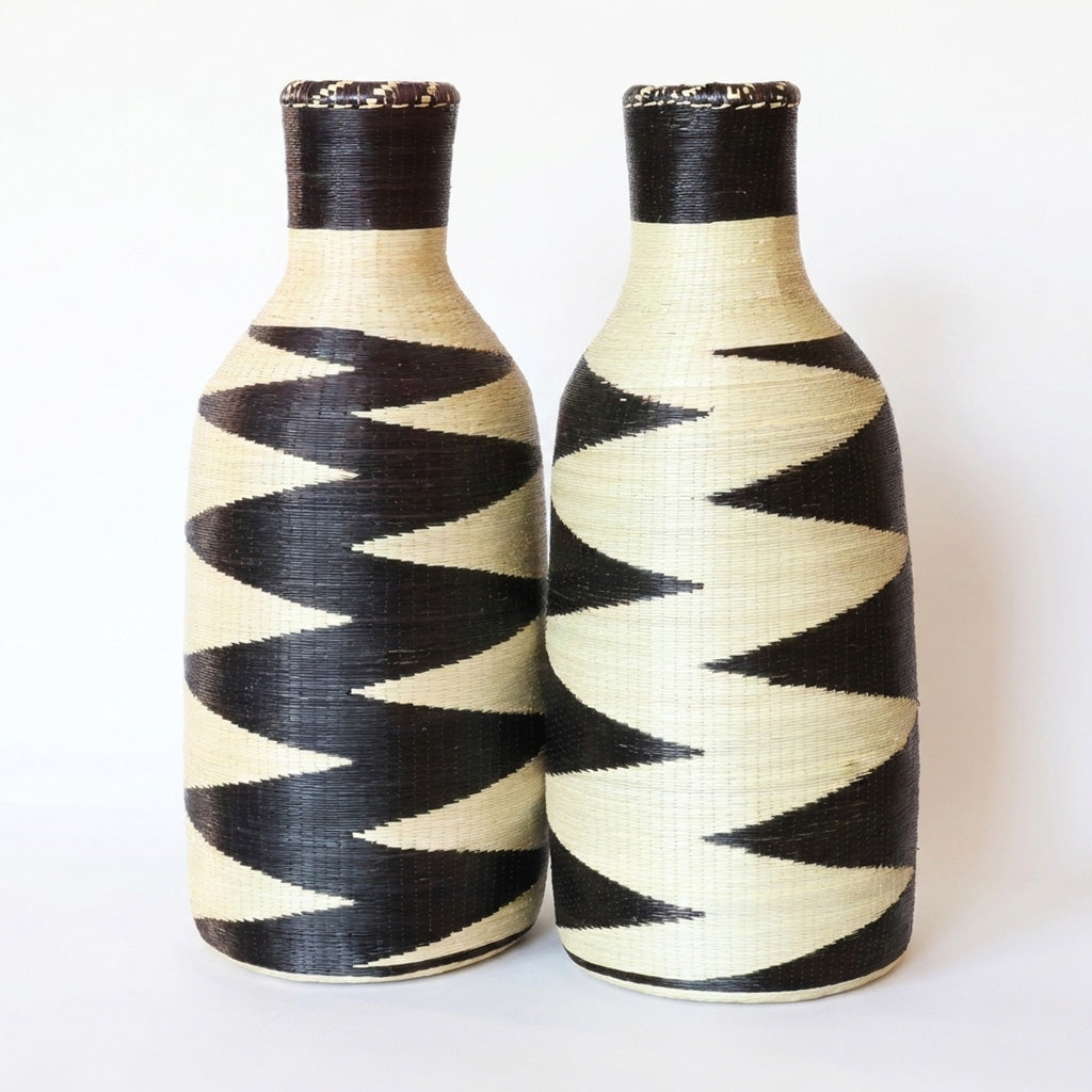 Pair of tall woven bottle vessels with black and cream zigzag patterns on white