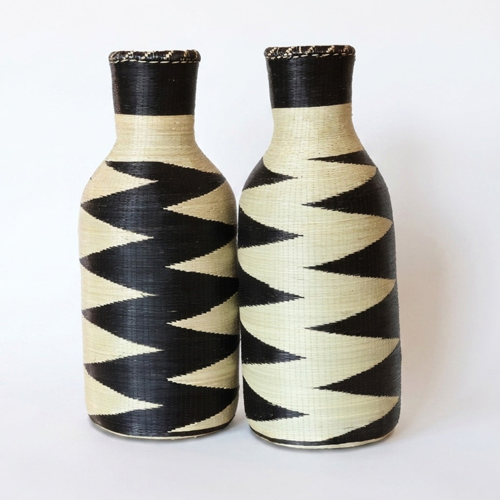 Pair of tall woven bottle vessels with black and cream zigzag patterns on white