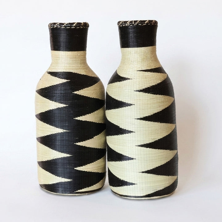 Pair of tall woven bottle vessels with black and cream zigzag patterns on white