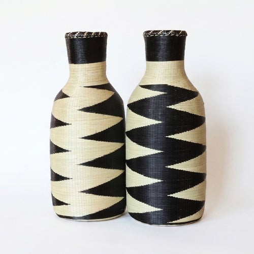 Pair of tall woven bottle vessels with black and cream zigzag patterns on white