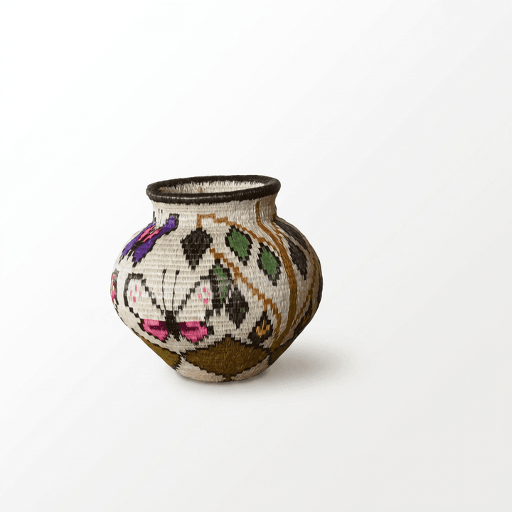 Side view of Wounaan butterfly basket showing rose-pink butterfly and woven green leaf diamonds on cream