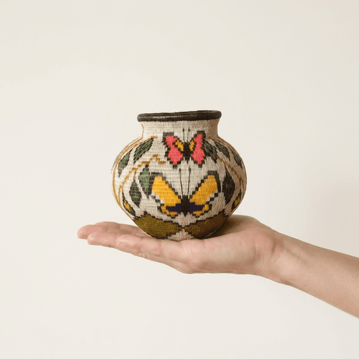 Handwoven Wounaan basket held in hand showing miniature scale, pink and yellow butterflies with leaves on cream