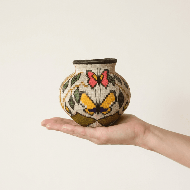 Handwoven Wounaan basket held in hand showing miniature scale, pink and yellow butterflies with leaves on cream