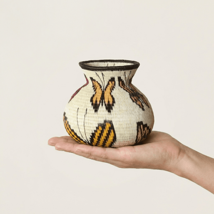 Ivory handwoven Wounaan butterfly basket with orange monarch wings held in hand showing miniature scale