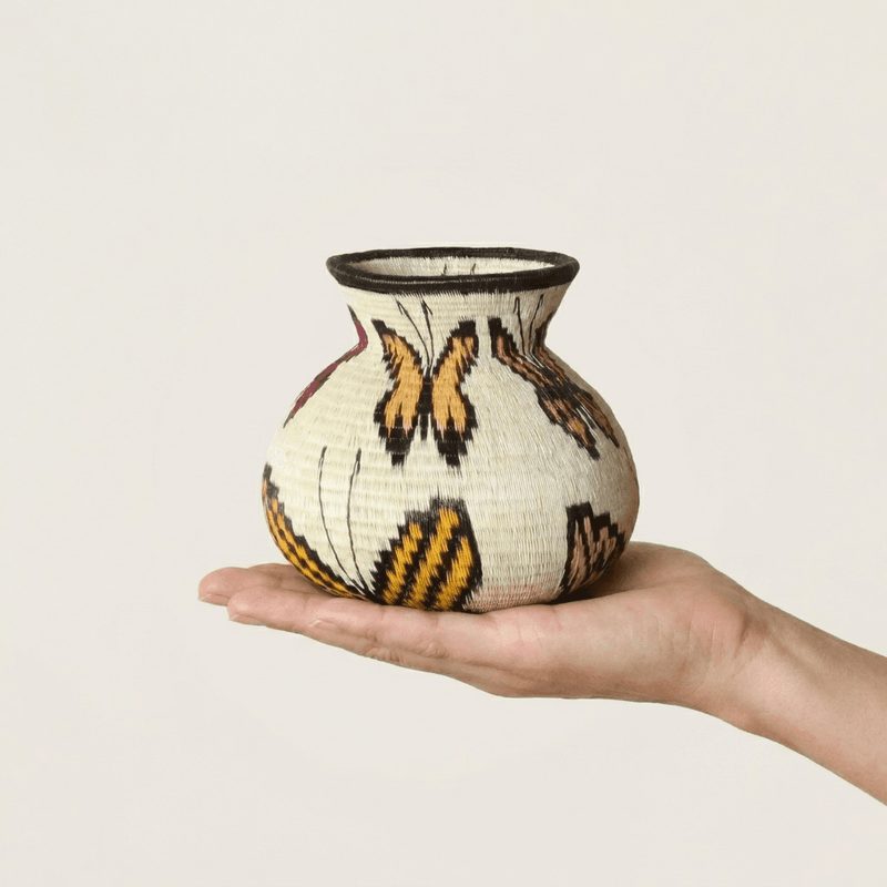 Ivory handwoven Wounaan butterfly basket with orange monarch wings held in hand showing miniature scale