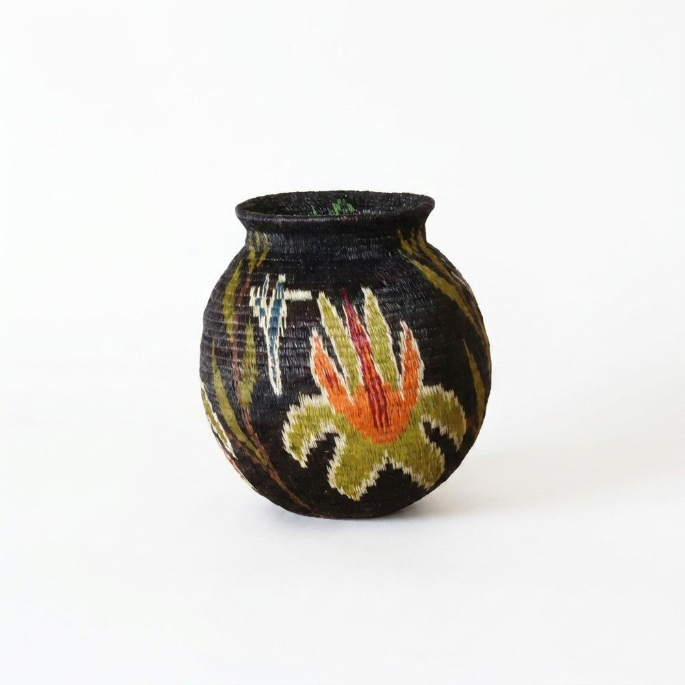Black handwoven Wounaan basket from Panama with flame-orange lily blossom and olive star leaves