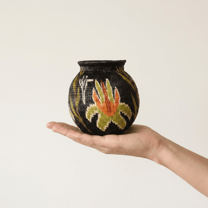 Black handwoven Wounaan basket with orange flame blossom held in hand showing miniature scale