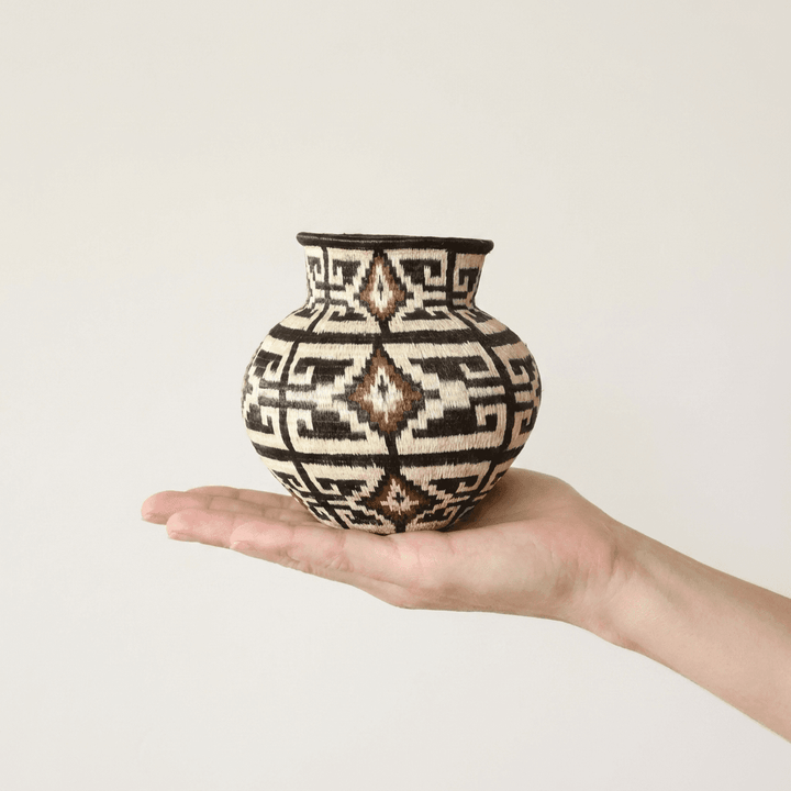 Geometric espresso-and-ivory handwoven Wounaan basket held in hand showing miniature scale