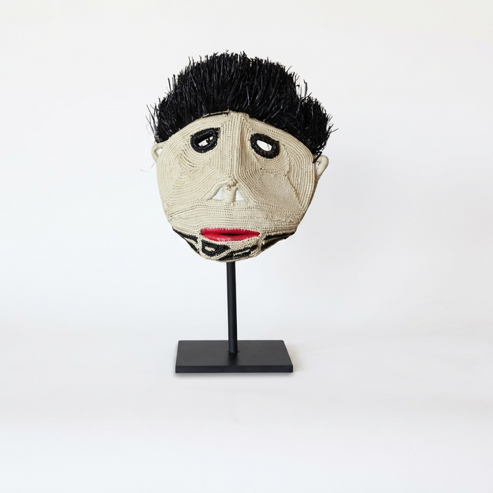 Handwoven Emberá spirit face mask in pale fiber with a dark crest and red mouth, from Panama