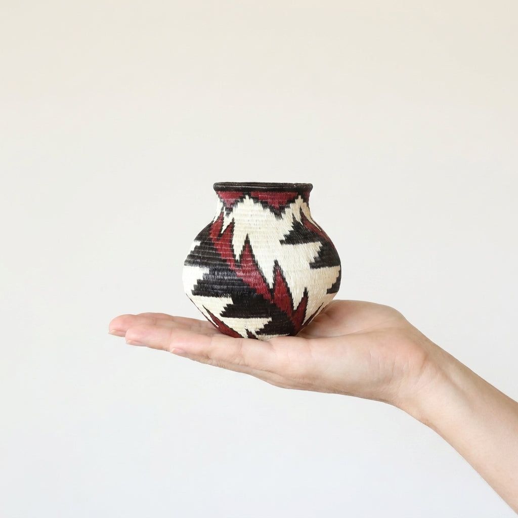 Crimson feather handwoven Wounaan basket held in hand showing miniature scale, about 4 inches tall