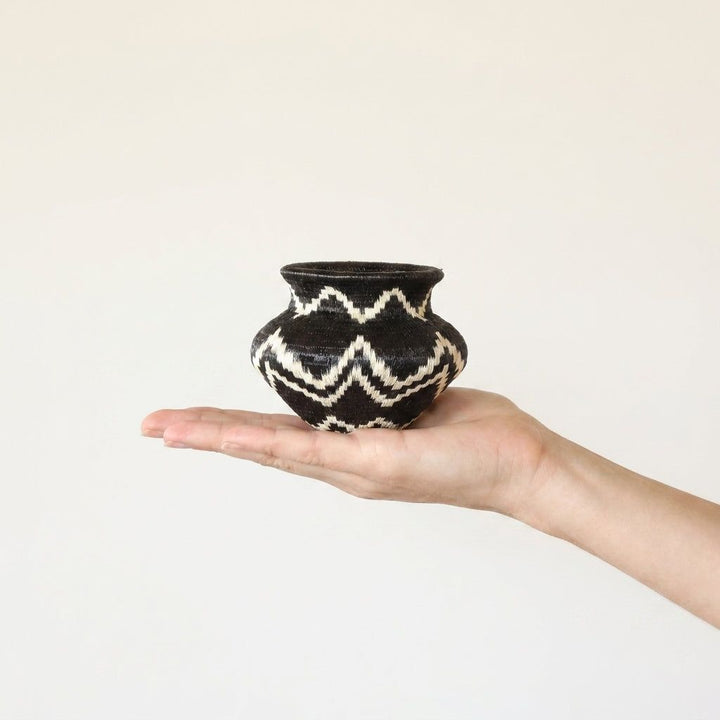 Geometric handwoven Wounaan basket held in hand showing miniature scale, black with ivory zigzags