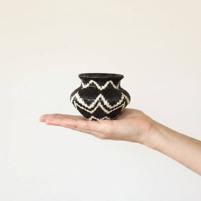 Geometric handwoven Wounaan basket held in hand showing miniature scale, black with ivory zigzags