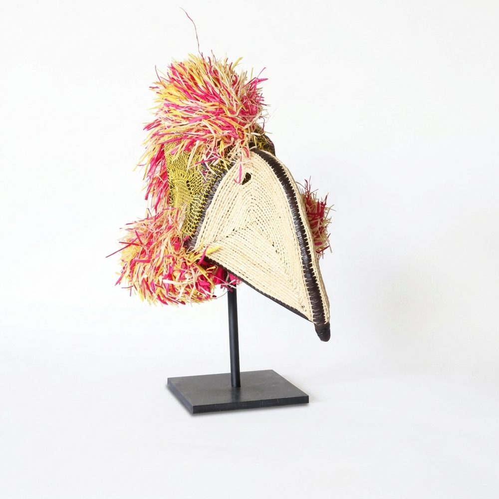 Emberá parrot spirit mask angled view showing shaggy crimson and yellow raffia crest, palm fiber wall art
