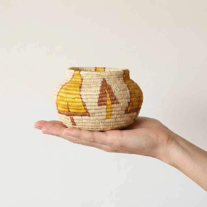 Small handwoven palm fiber basket with golden tree pattern by village artisans