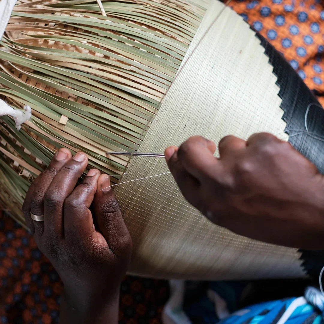 Rwandan artisan's hands stitching a coiled basket with a needle