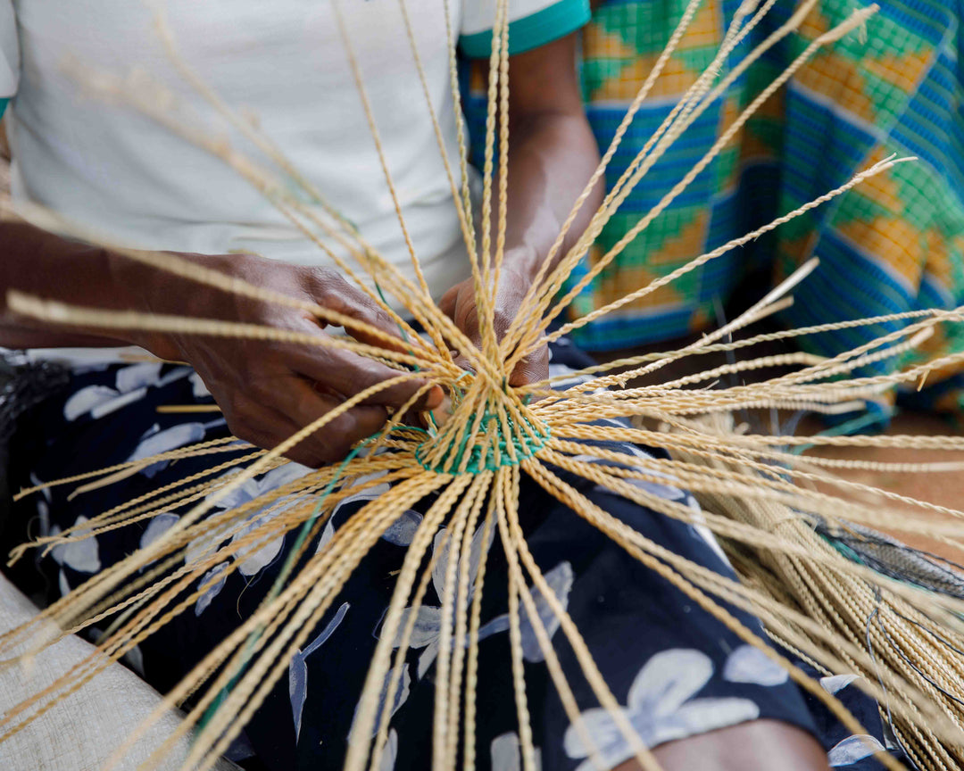 Bolga weaver starting a new basket, twisted strands of elephant grass radiating from the center, Bolgatanga, Upper East Region, Ghana
