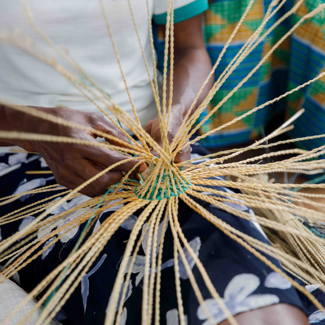 Bolga weaver starting a new basket, twisted strands of elephant grass radiating from the center, Bolgatanga, Upper East Region, Ghana